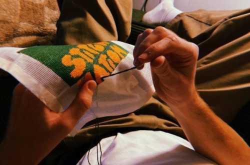 A person relaxing on a couch, carefully embroidering a colorful design on fabric.