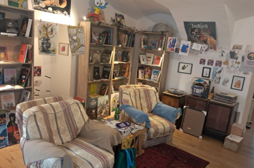 A cozy reading and creative space with bookshelves, armchairs, and various artworks decorating the walls.