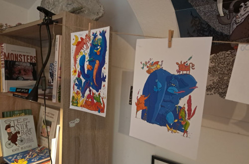 Colorful illustrations hanging on a string, displayed in a creative workspace with books and art materials.