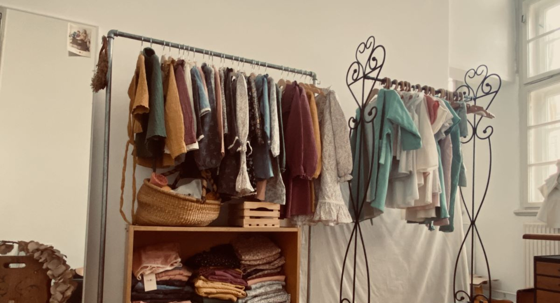 Une boutique ou un showroom exposant des vêtements faits main au style vintage sur des portants en métal, avec des textiles soigneusement pliés sur des étagères en bois.