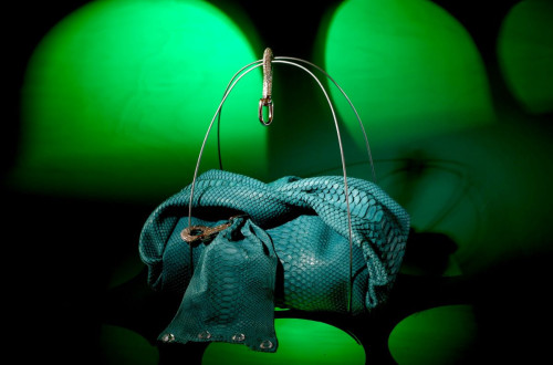 A striking turquoise handbag with a snakeskin texture, displayed under green lighting.