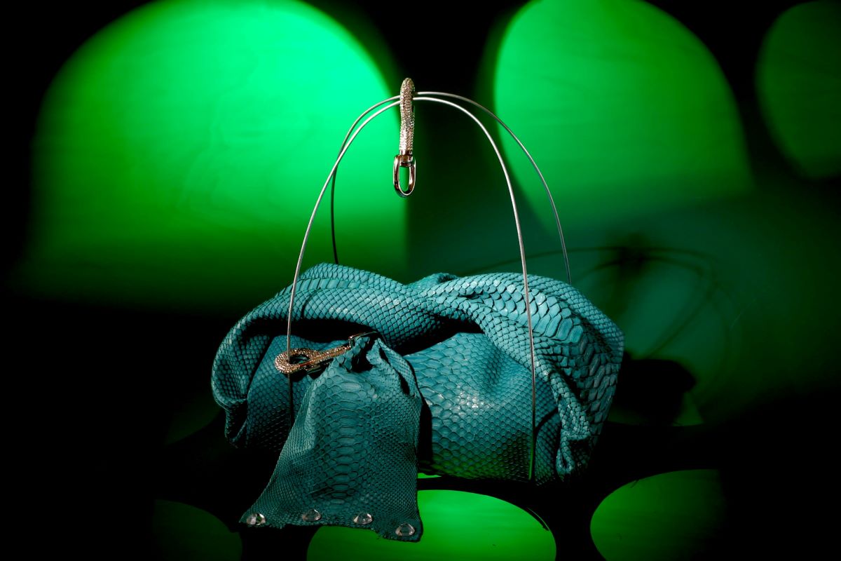 A striking turquoise handbag with a snakeskin texture, displayed under green lighting.