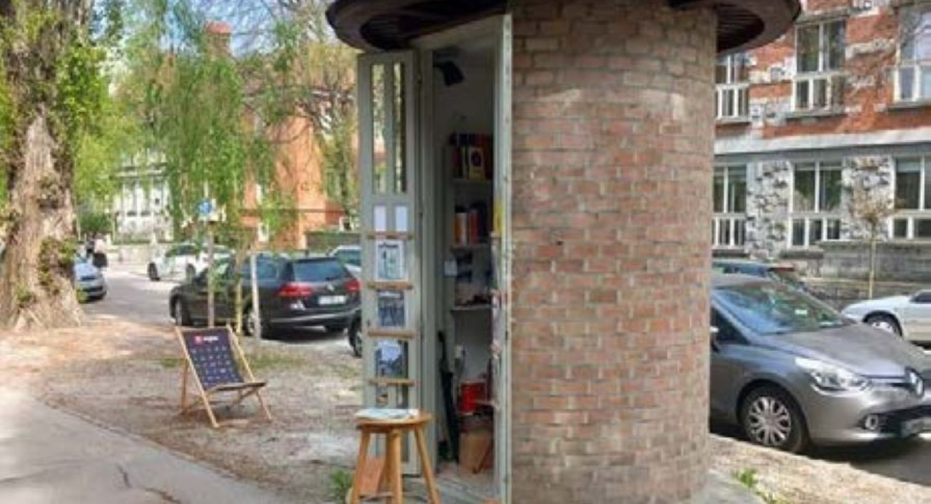 A small, round brick structure repurposed as a free outdoor library, with bookshelves inside and a chair nearby.