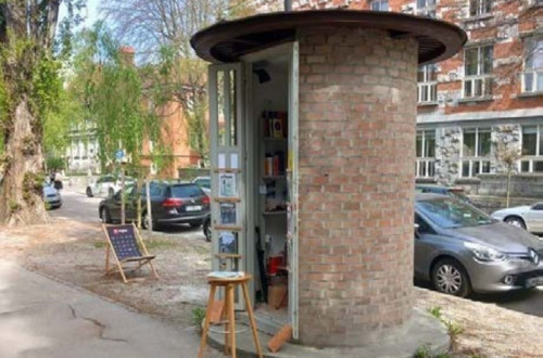 A small, round brick structure repurposed as a free outdoor library, with bookshelves inside and a chair nearby.