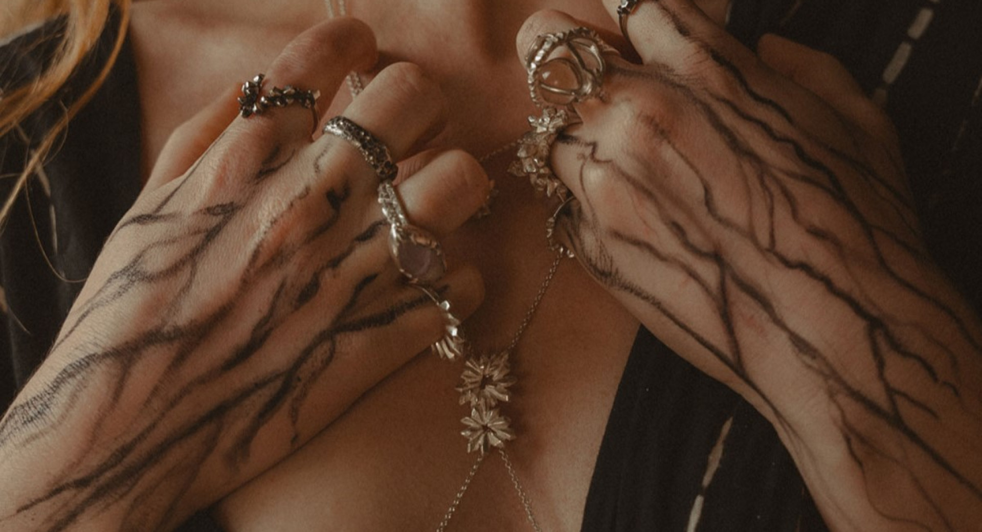 A close-up of hands adorned with intricate metal jewelry, featuring rings and a delicate necklace.