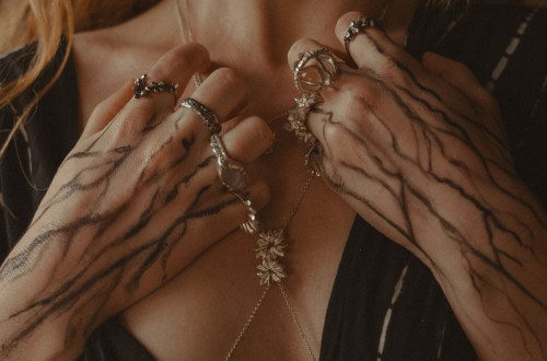 A close-up of hands adorned with intricate metal jewelry, featuring rings and a delicate necklace.