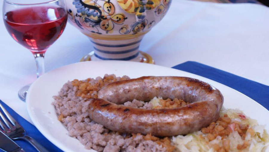 Grilled sausage with sauerkraut and buckwheat porridge. Served alongside the dish are a small jug and a glass of wine.