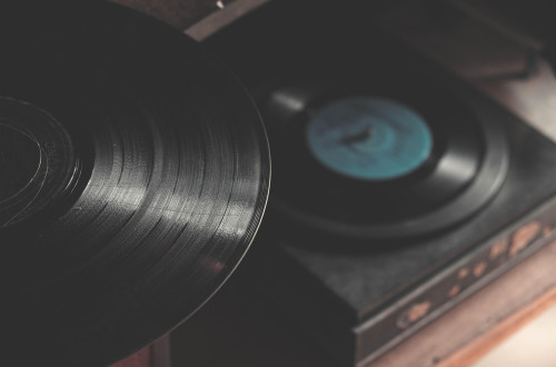 Close-up of a black vinyl record being held over a turntable, on which there is another record.