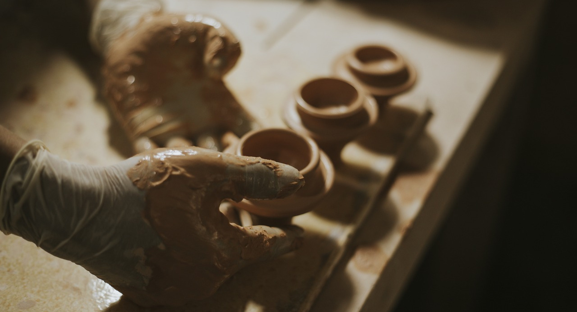 A person makes a small clay pot in their studio.