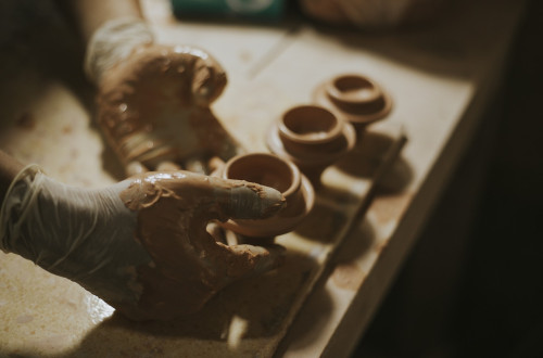 A person makes a small clay pot in their studio.