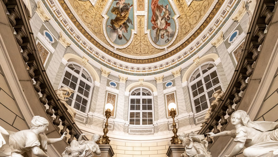 A woman sitting on a staircase. A glorious ceiling above her.