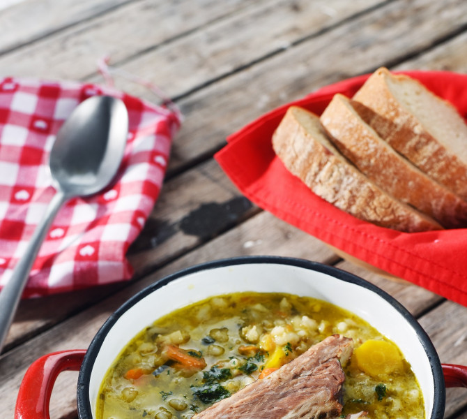 Pot with stew in the foreground. Slices of bread in the background.
