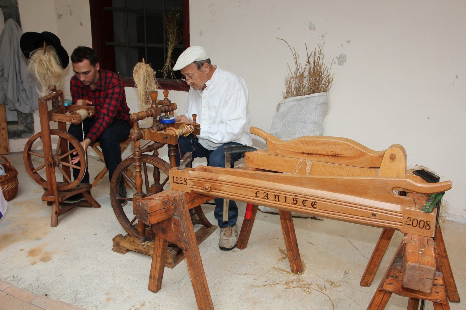 Two men sitting beside a wooden flax spinning device.