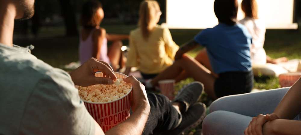 A group of people sitting on the lawn and watching a movie.