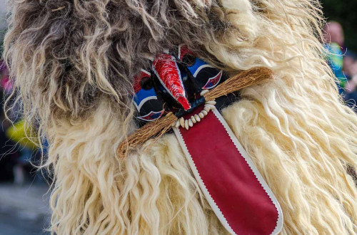 The traditional mask with coarse wool in light and dark shades is adorned with a long red tongue, vivid colours and small details.