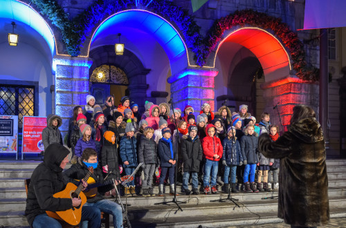 Otroški pevski zbor na stopnicah pred mestno hišo v času Prazničnega decembra.