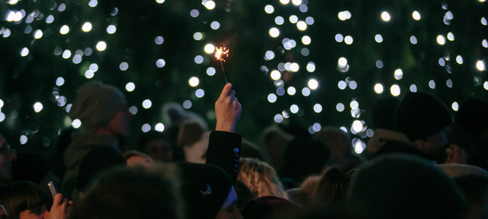 Person holding up a sparkling candle, decorated christmas tree.