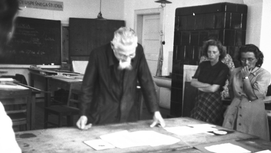 A black and white photo of a man leaning over the table. Architectural plans on it.