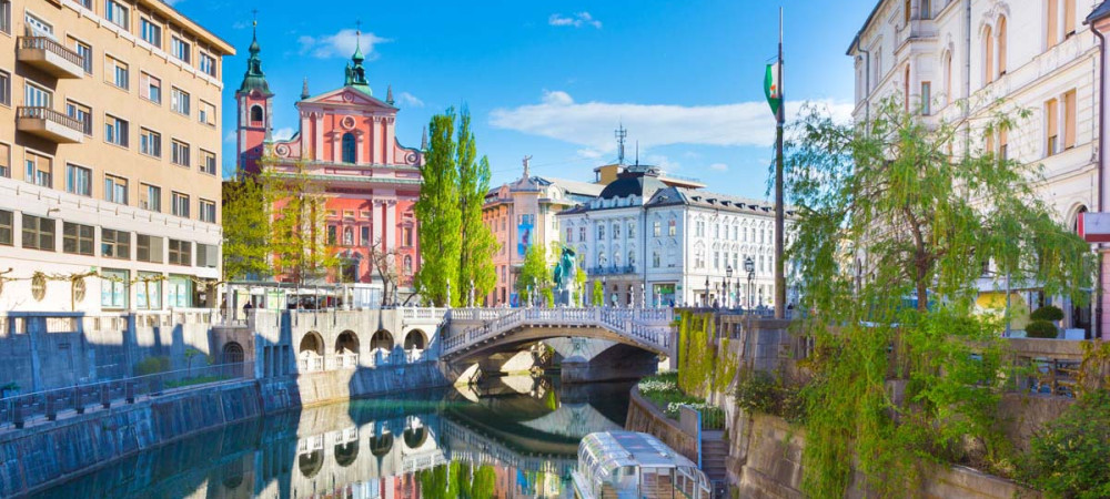 Razgled iz mostu na turistično ladjo na Ljubljanici. V ozadju Tromostovje in Prešernov trg.