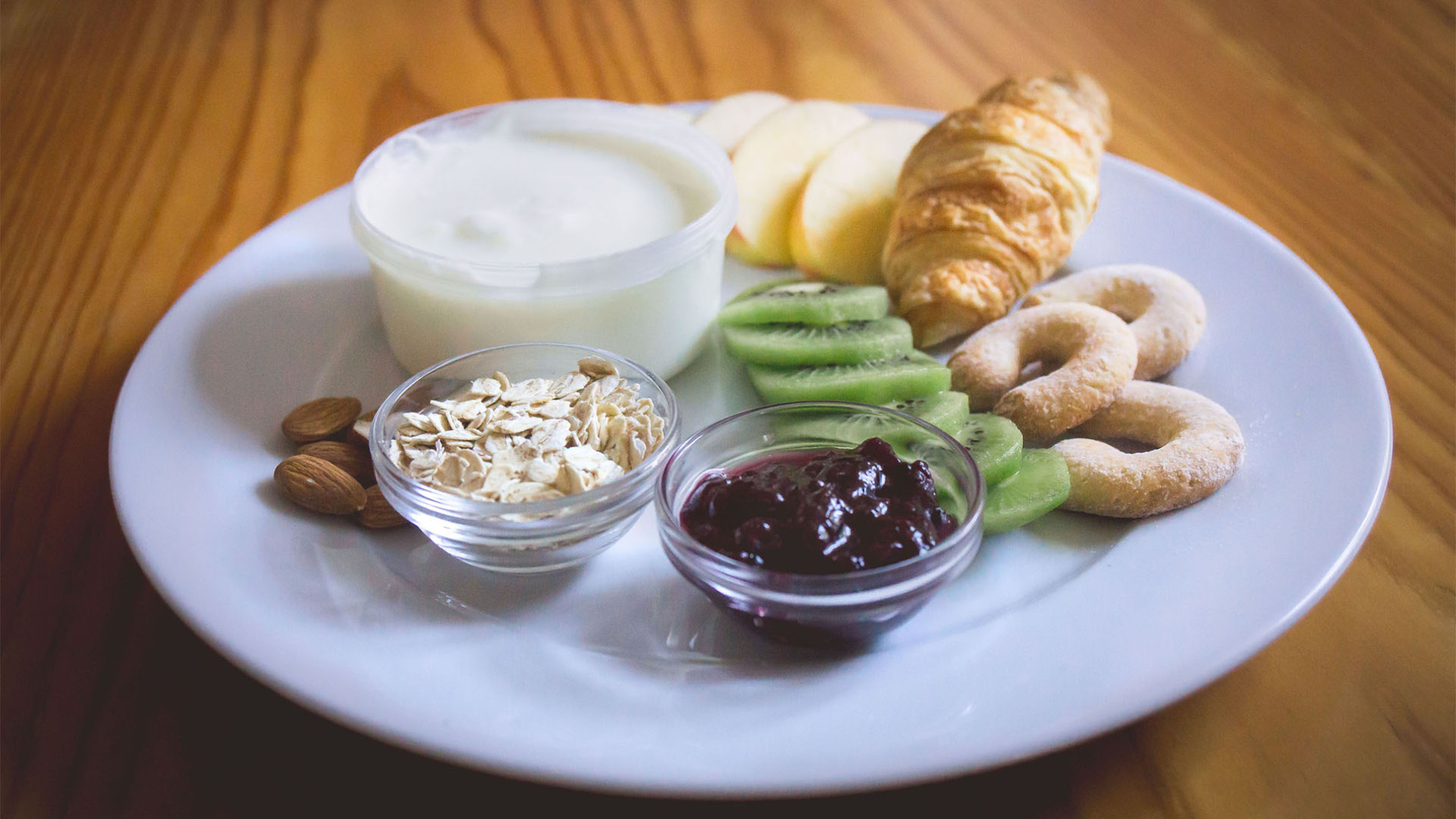 Zajtrk. Rogljiček, marmelada, jogurt in kosmiči na krožniku.