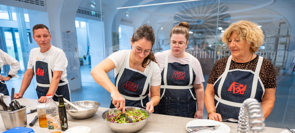 Two men and three women in black aprons are preparing food at the table.