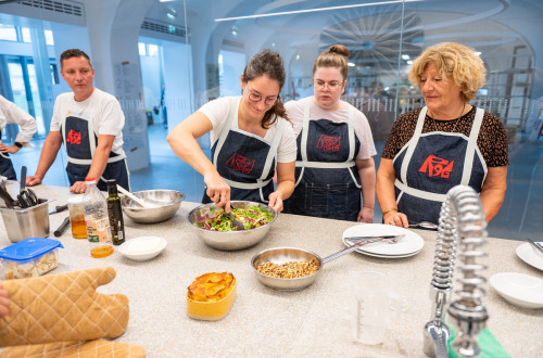 Two men and three women in black aprons are preparing food at the table.