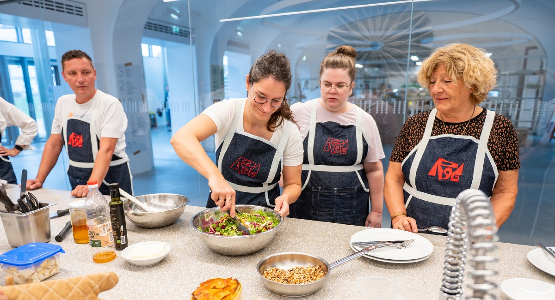 Two men and three women in black aprons are preparing food at the table.